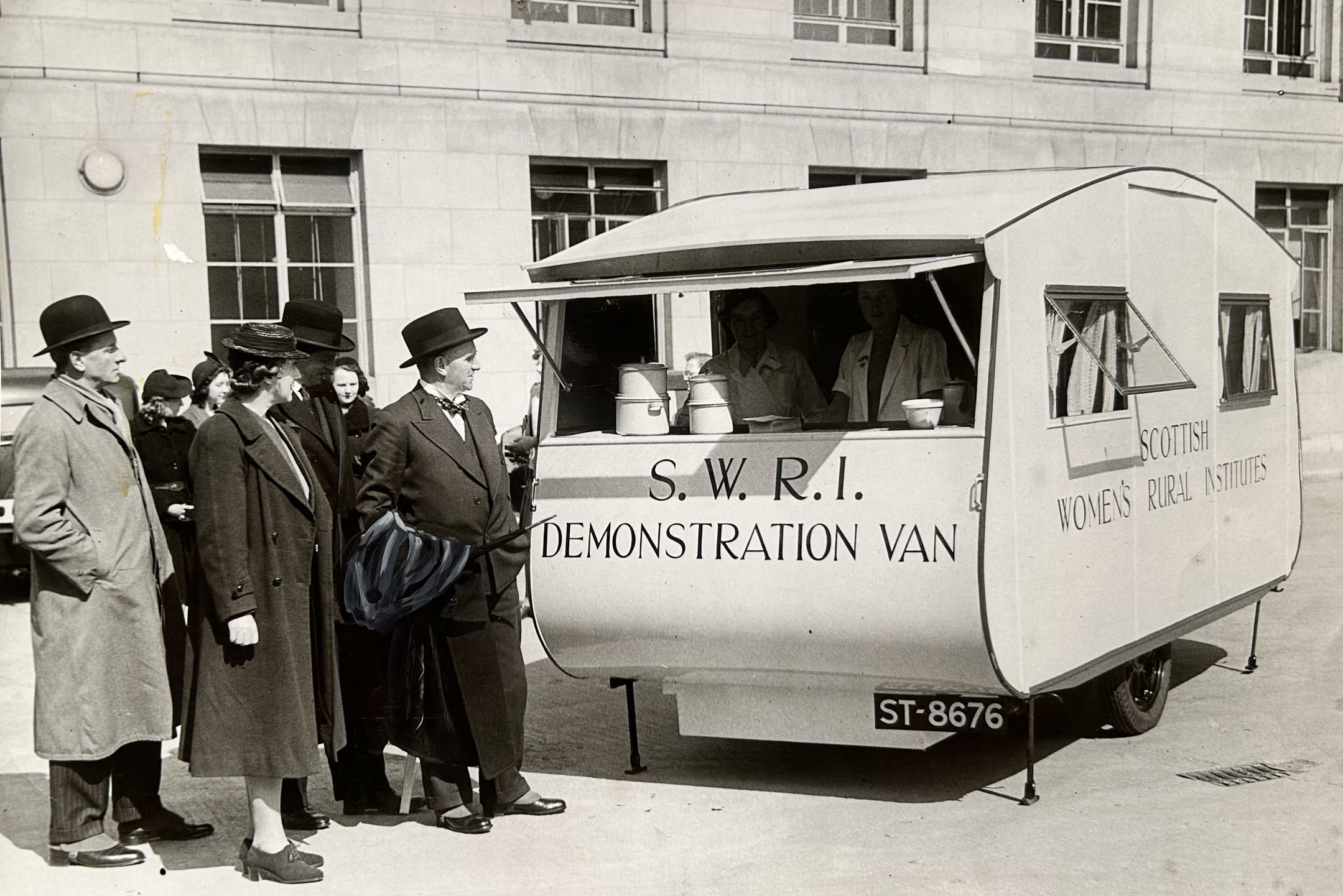A black and white photo of an SWRI Demonstration Van outside of a building, there is a group of people standing by.